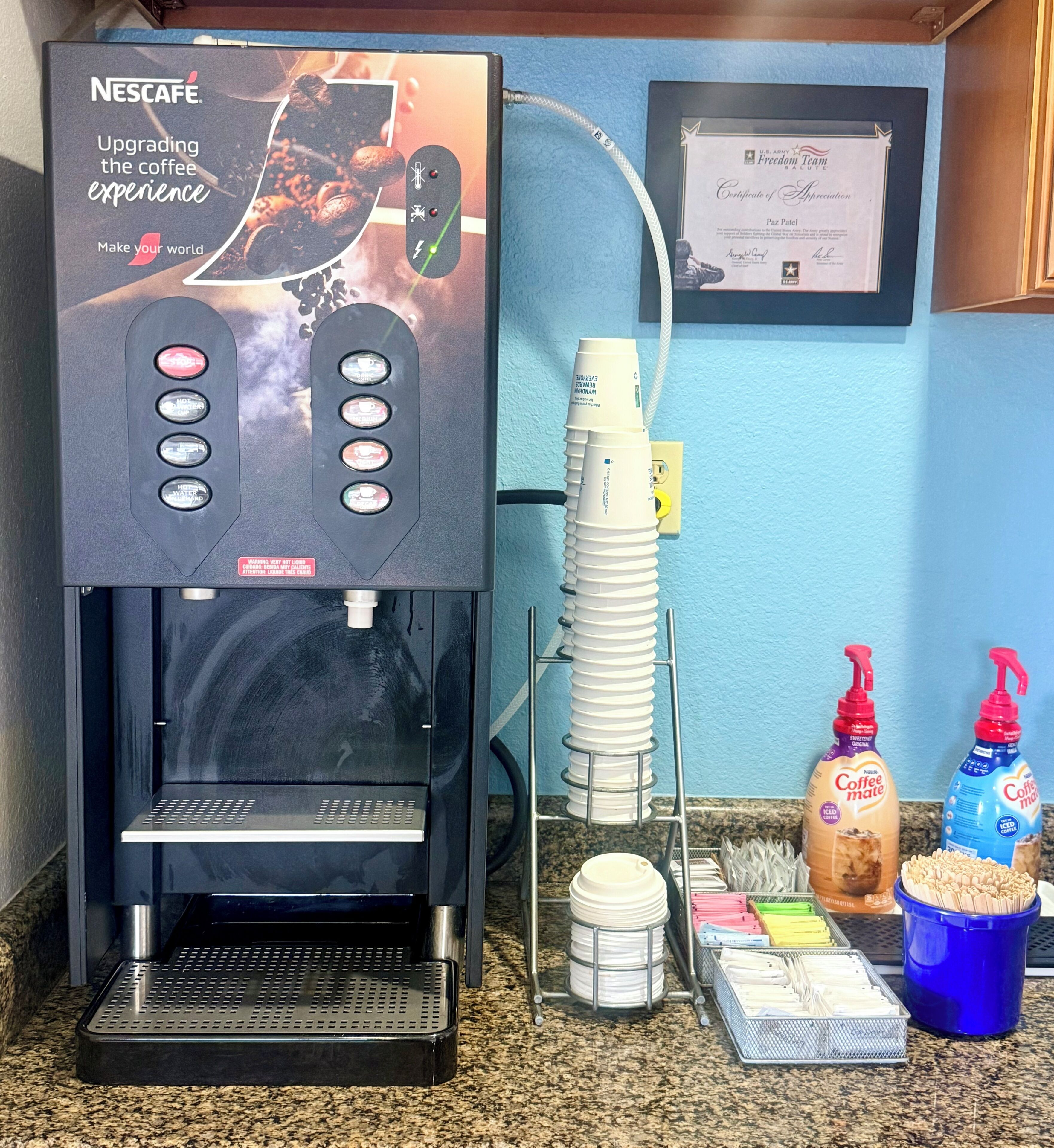 A Nescafe coffee machine with a menu display, a certificate of appreciation, and coffee-making supplies on a countertop.