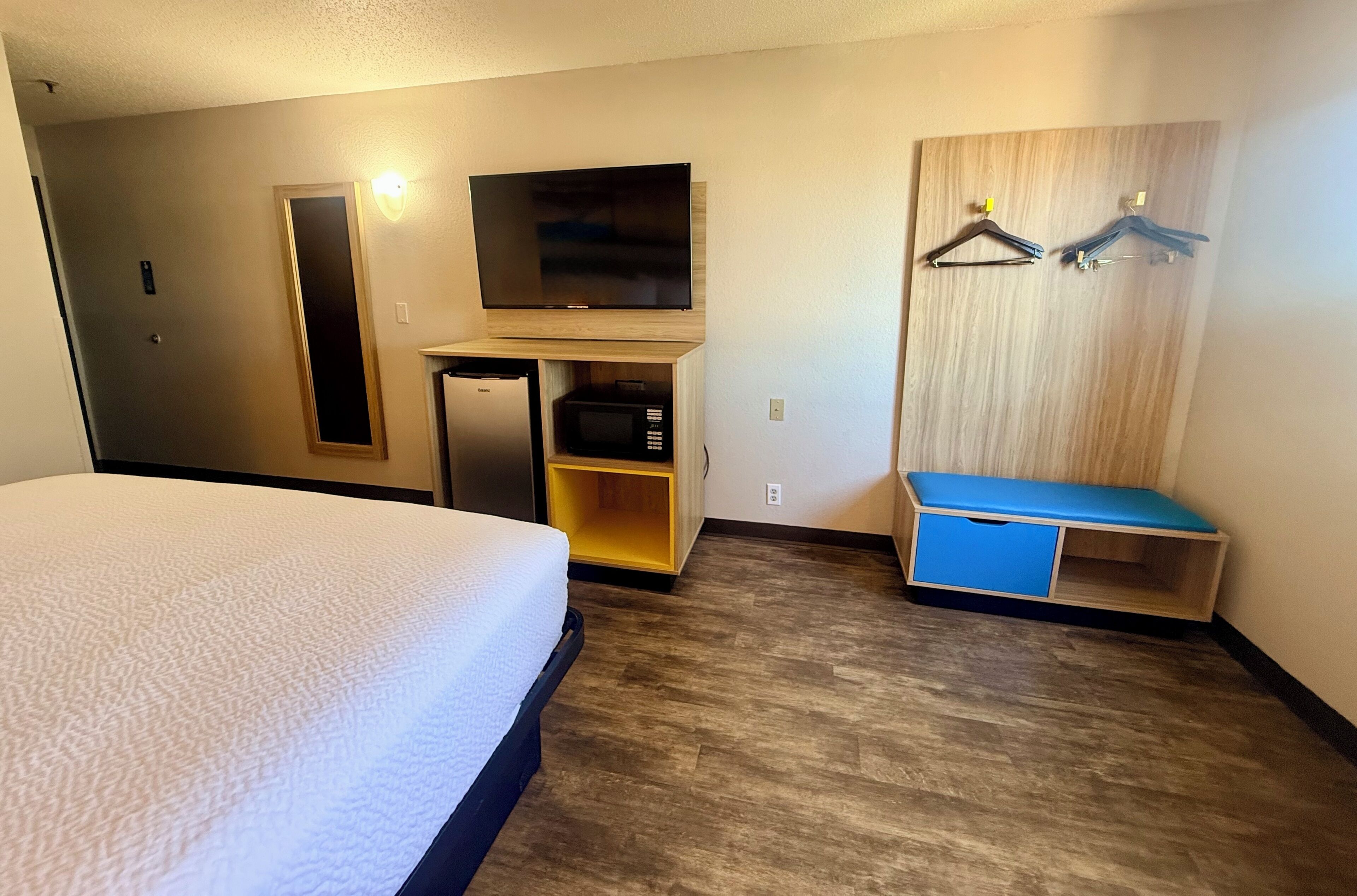 Una habitación de hotel con cama, televisor, microondas y armario de madera con banco.
