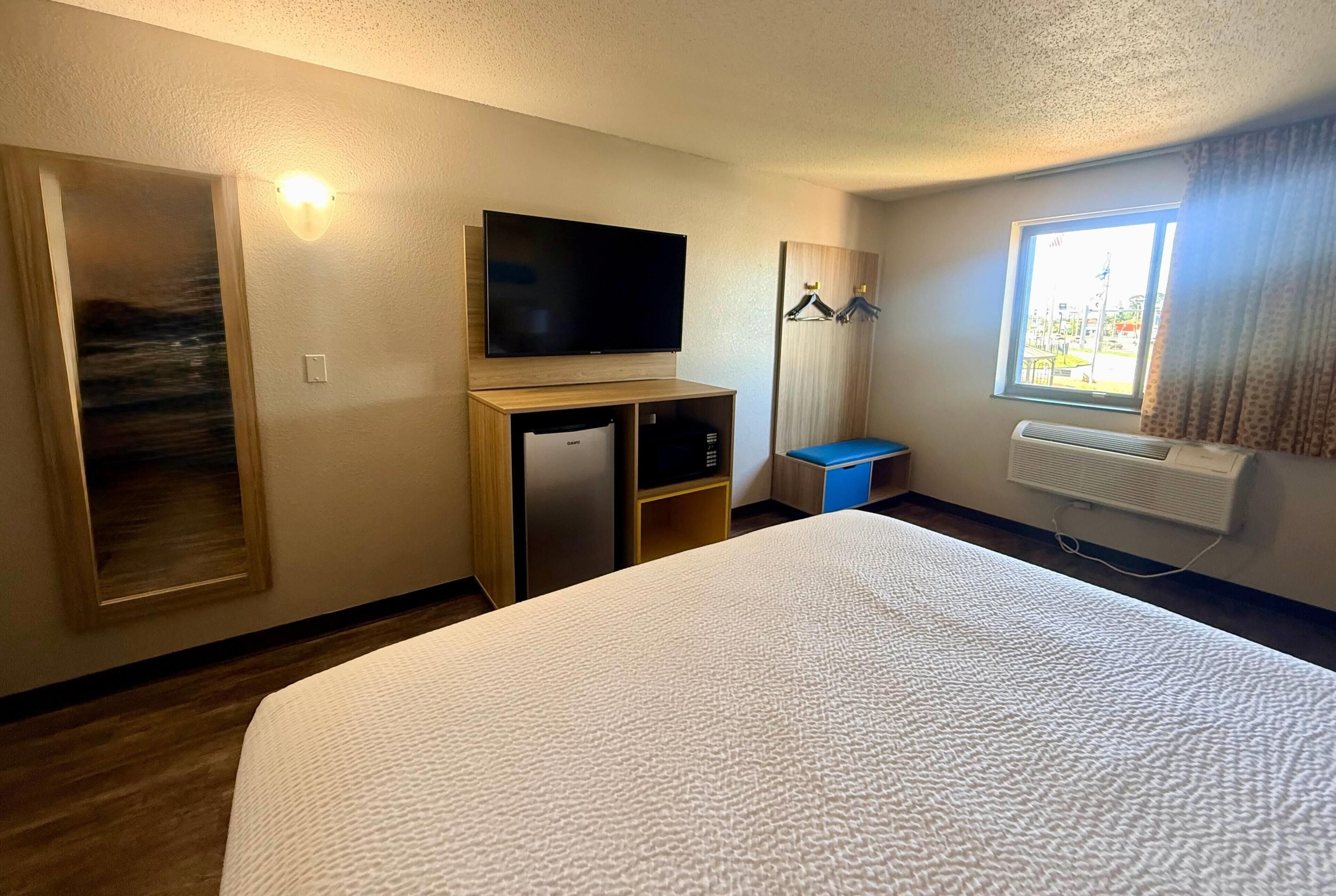 Habitación de hotel con cama, televisión, escritorio, armario, ventana con cortinas y radiador.