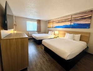 Quarto de hotel com duas camas, uma escrivaninha, uma televisão de tela plana, um quadro e uma janela com cortinas.