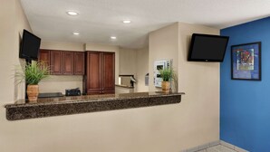 A reception area with a counter, wooden cabinets, a flat-screen TV, and a framed picture on the wall. - Days Inn by Wyndham Orange Park/Jacksonville (Orange Park)