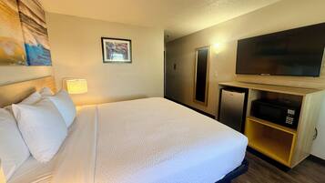 Una habitación de hotel con cama, televisión, microondas y un mueble pequeño.