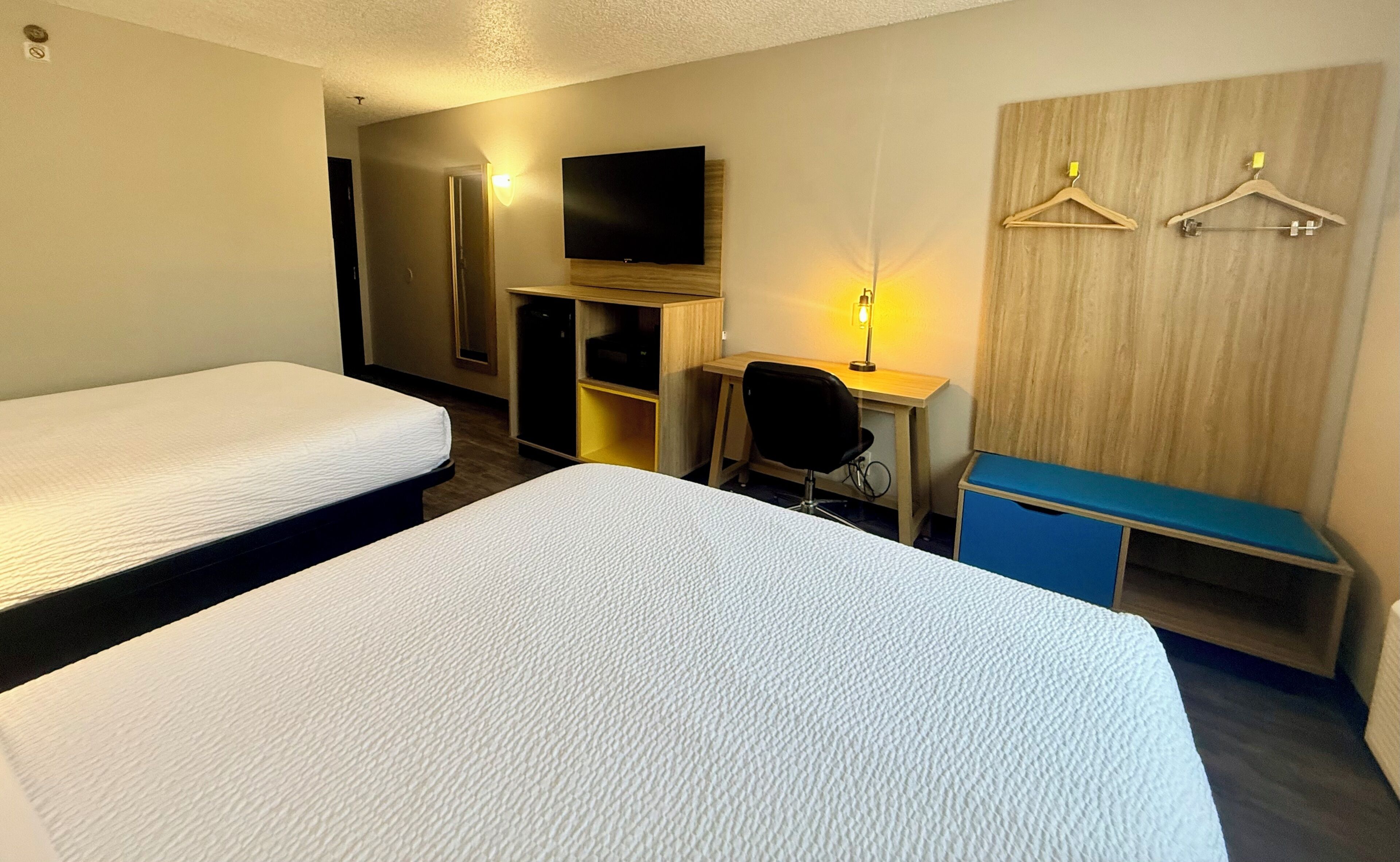 A hotel room with two beds, a desk with a chair, a television, and a wardrobe.