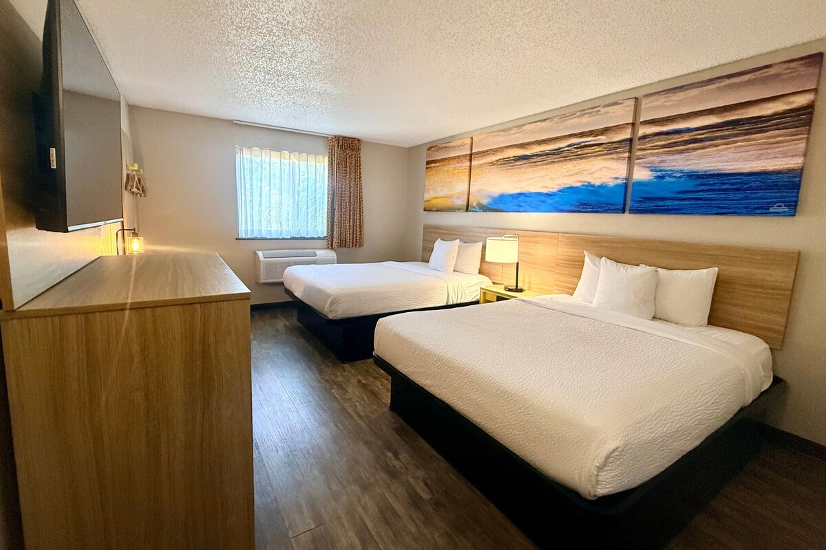 A hotel room with two beds, a large painting, a mirror, and a desk.