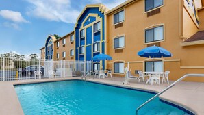 A swimming pool with a white fence, blue umbrellas, and white chairs. - Days Inn by Wyndham Orange Park/Jacksonville (Orange Park)