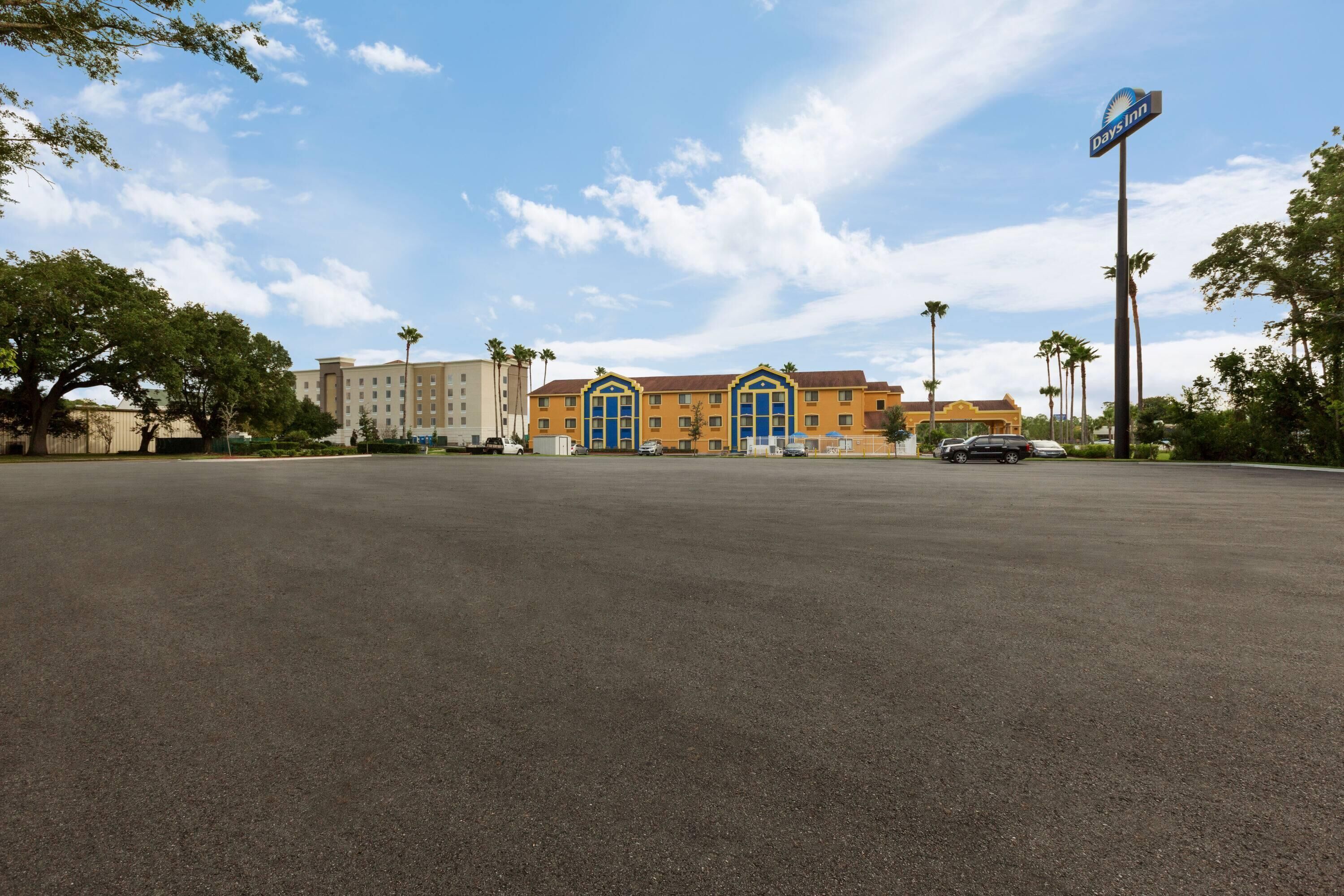 A Days Inn with a large parking lot, a building with blue-framed windows, and palm trees in the background.
