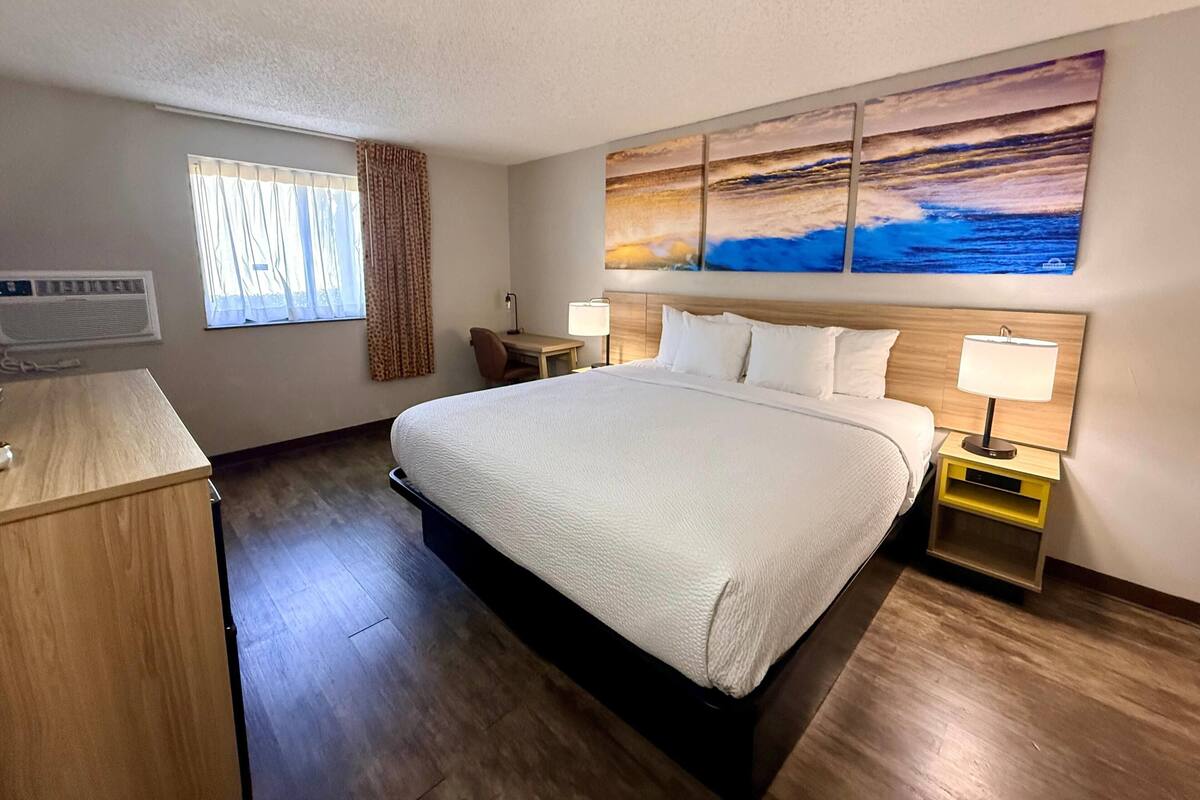 A hotel room with a large bed, bedside tables, a desk, and a window with curtains.