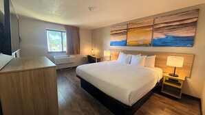 A hotel room with a bed, bedside tables, a desk, a TV, and a window with curtains. - Days Inn by Wyndham Orange Park/Jacksonville (Orange Park)