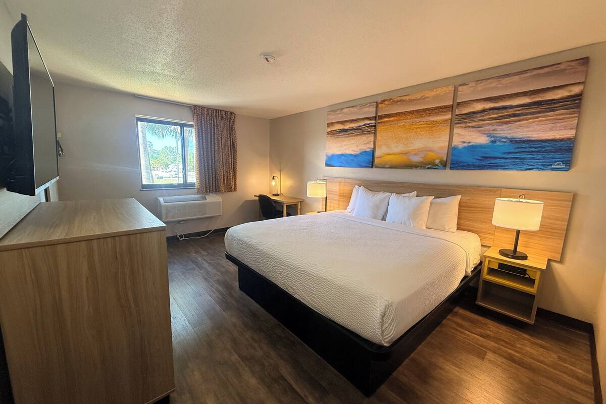 A hotel room with a bed, bedside tables, a desk, a TV, and a window with curtains.