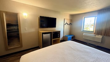 Une chambre d’hôtel équipée d’un lit, d’une télévision, d’un mini-réfrigérateur, d’un radiateur, d’une fenêtre avec des rideaux et d’un porte-manteau.