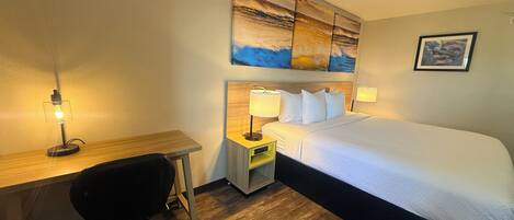 A hotel room with a bed, desk, chair, bedside lamps, and artwork on the wall.