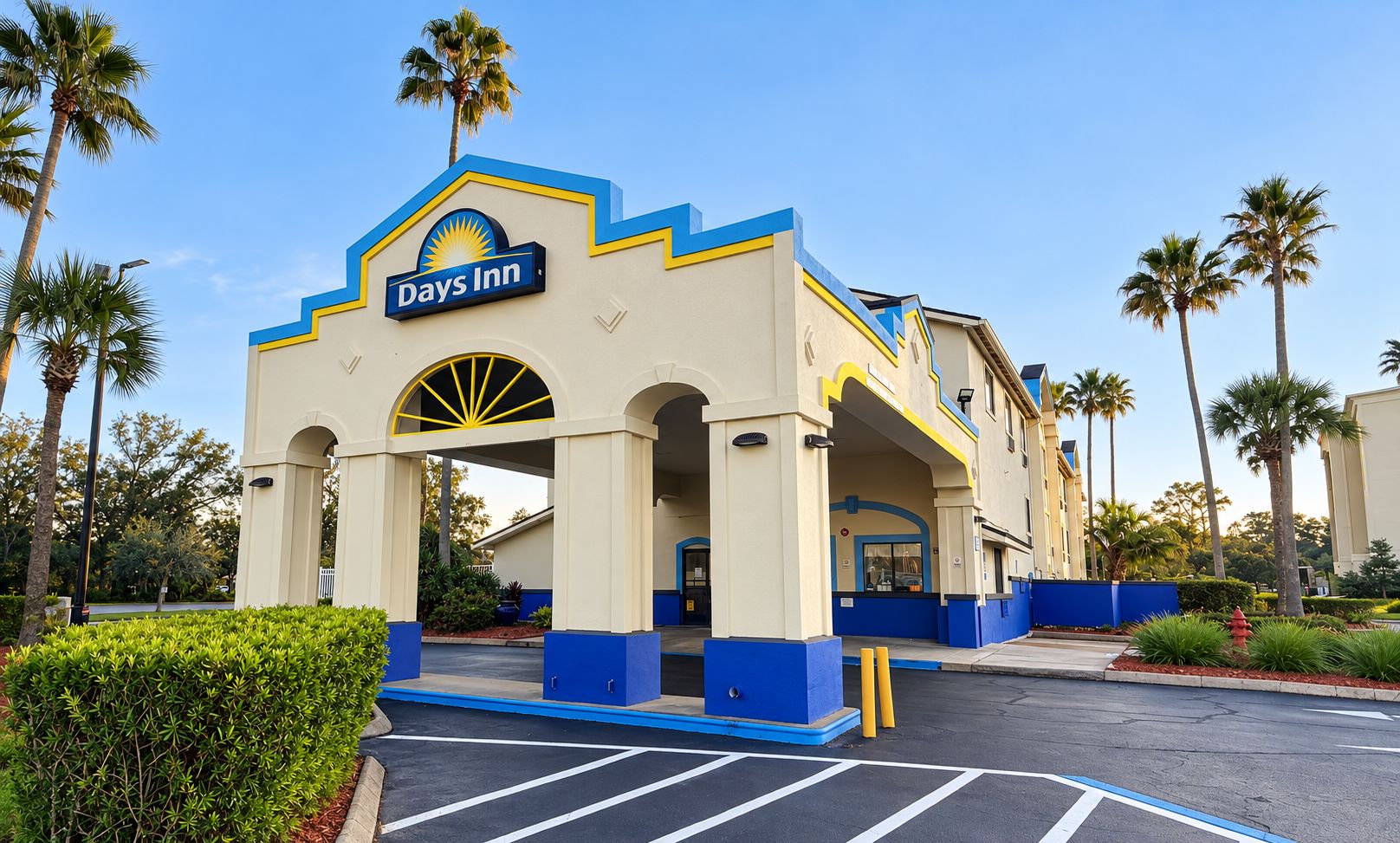 A Days Inn with a distinctive blue and yellow facade, a parking lot, and palm trees in the background.
