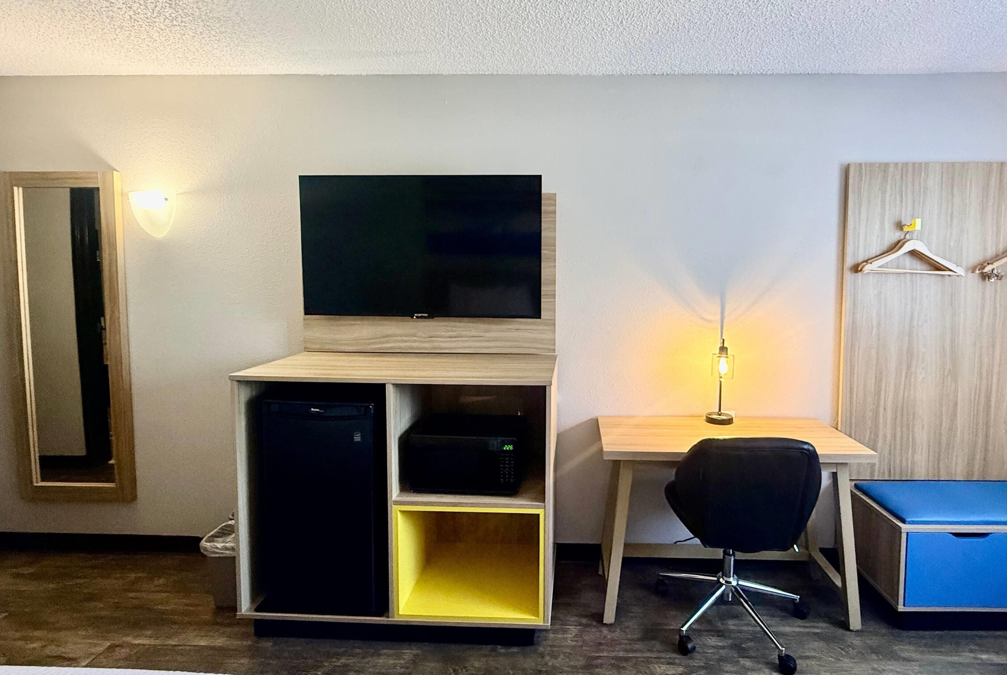 A room with a TV on a wooden stand, a desk with a chair, and a small cabinet.