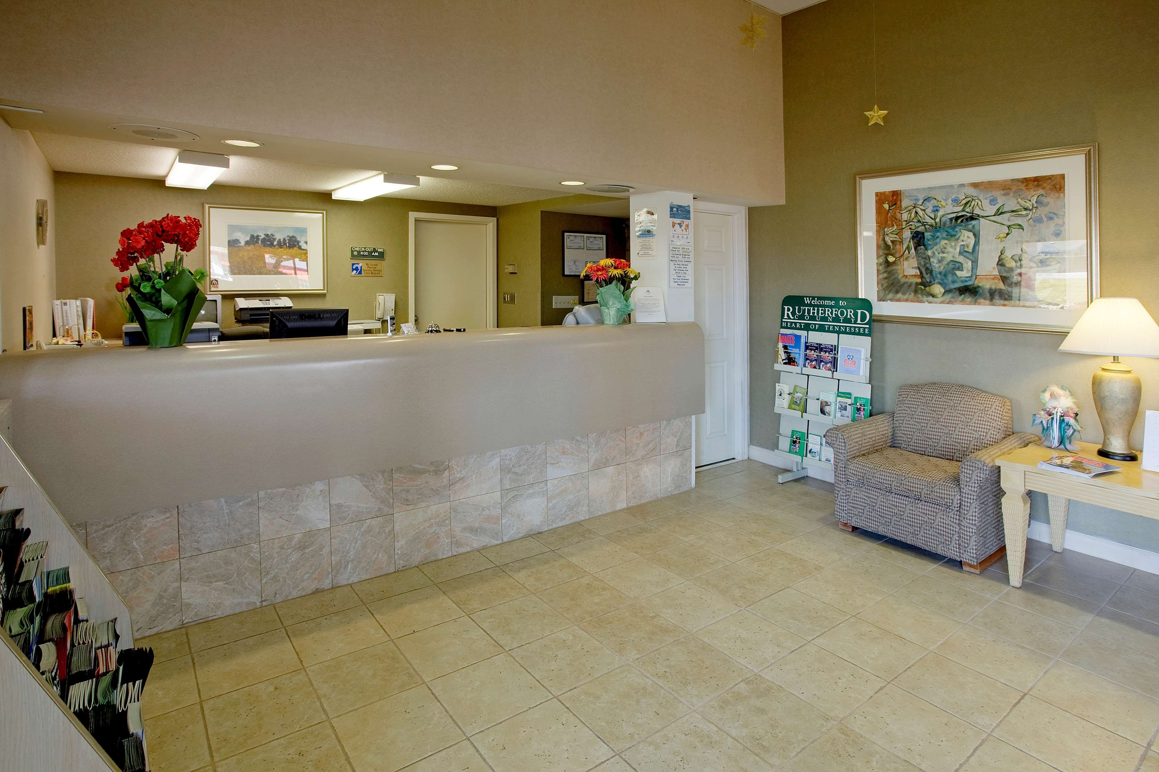 A reception area with a check-out counter, a chair, a desk with a lamp, and a framed welcome sign.