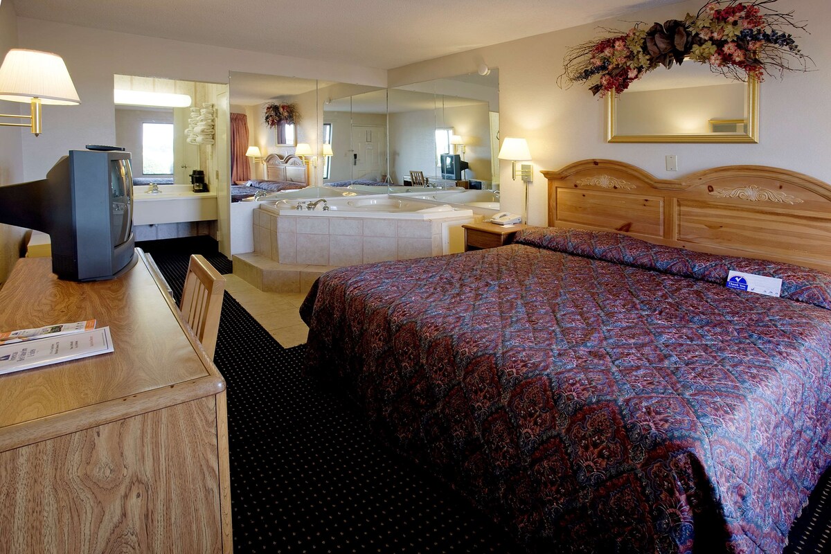 Ein Hotelzimmer mit Bett, Schreibtisch, Fernseher und einem Badezimmer mit Badewanne sowie einem Spiegel.