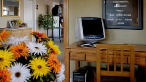 A hotel room with a wooden desk, a computer, and a floral arrangement. - Americas Best Value Inn & Suites Murfreesboro (Murfreesboro)