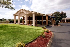 Ein Gebäude mit überdachter Eingangspartie und Parkplatz.