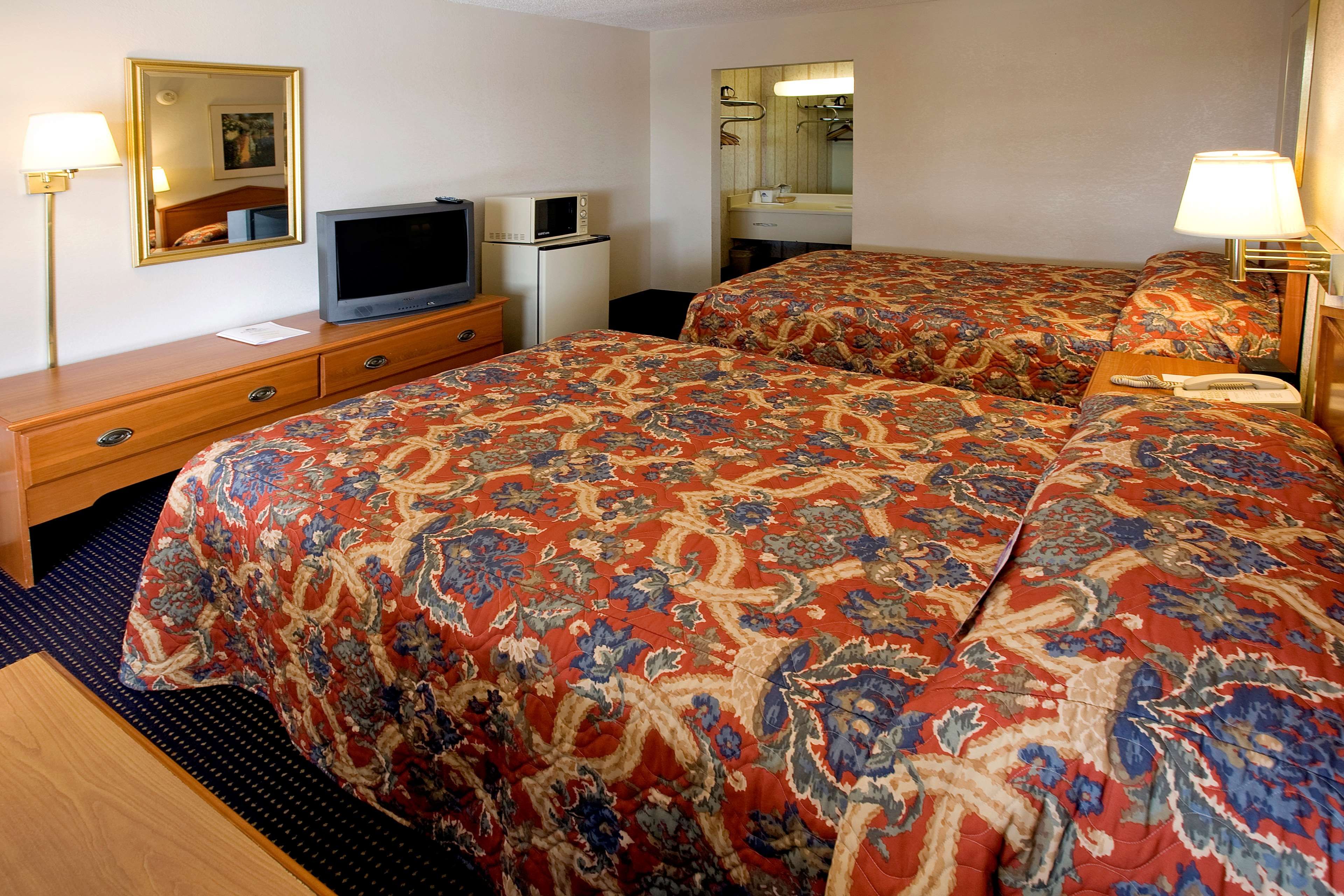A hotel room with a double bed, a television, a refrigerator, a bedside table, and a mirror.