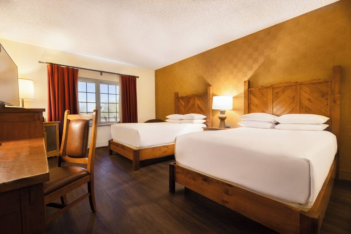 Habitación de hotel con dos camas, cabeceros de madera, un escritorio y una silla.