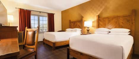 A hotel room with two beds, wooden headboards, a desk, and a chair.