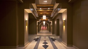A long, narrow hallway with patterned flooring, recessed lighting, and a central chandelier. - Eldorado Hotel & Spa (Santa Fe)