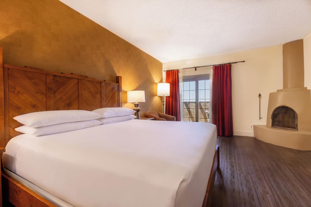 Una habitación de hotel con una cama grande, una chimenea, un ventanal con cortinas y un techo de madera.