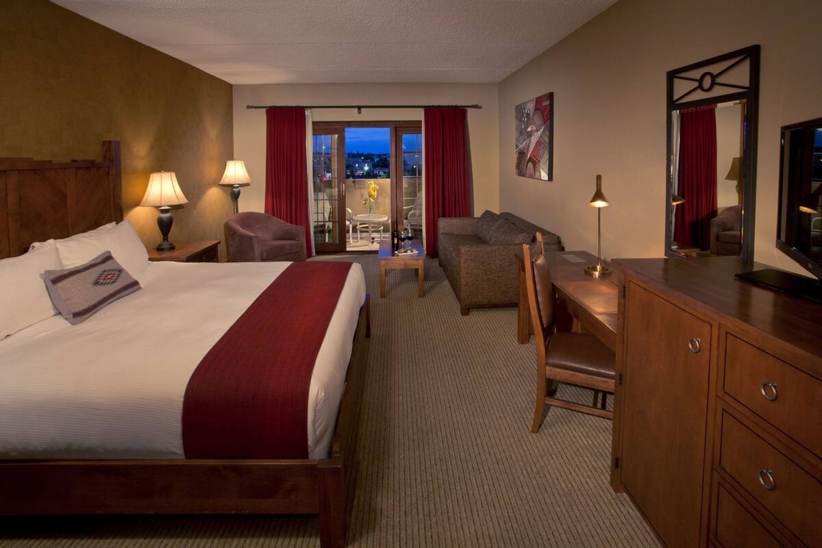 Habitación de hotel con cama, escritorio, silla y vista a la ciudad por la ventana.