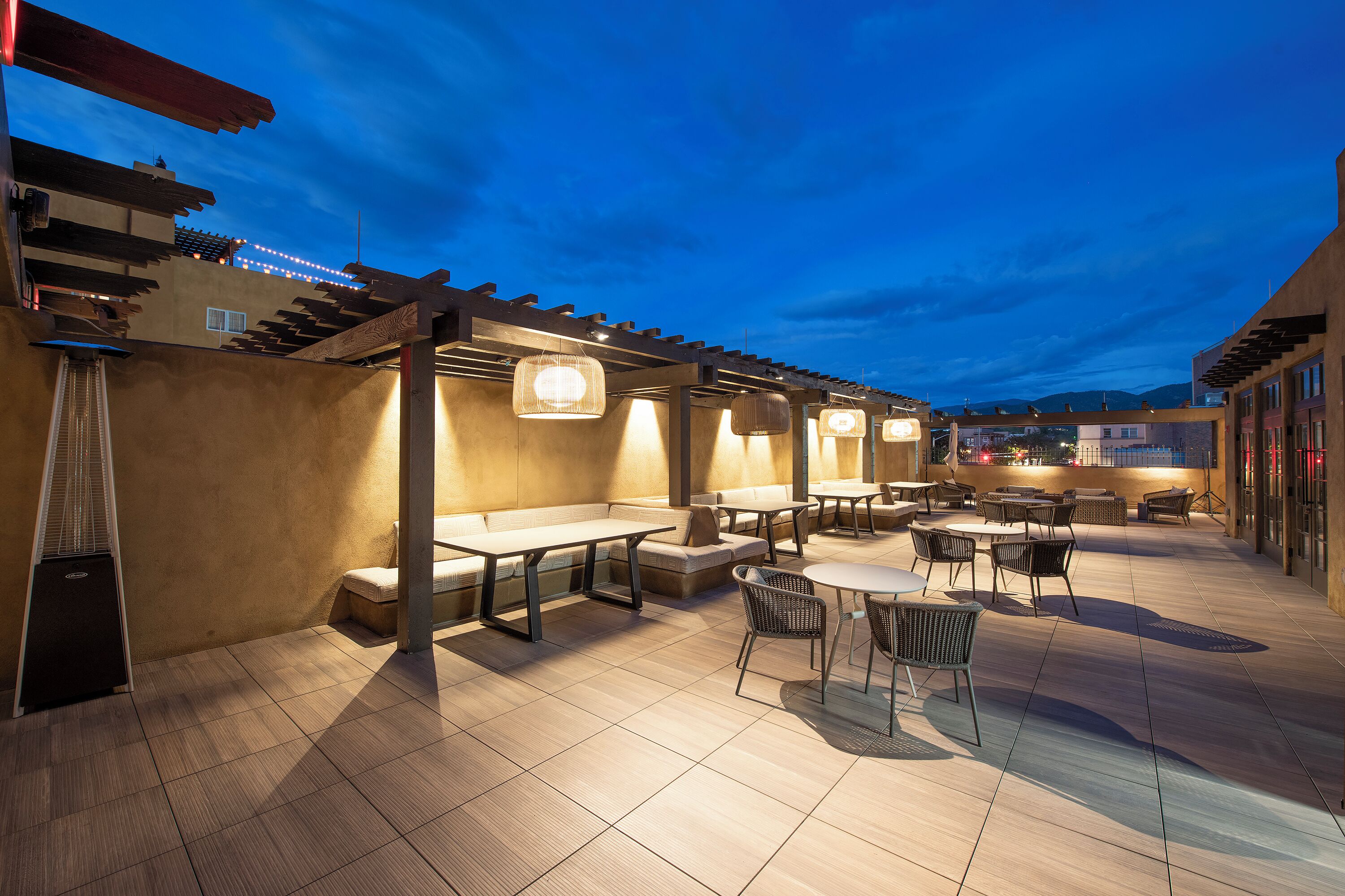 Un área de patio al aire libre con mesas y sillas, una pérgola y vistas de la ciudad.