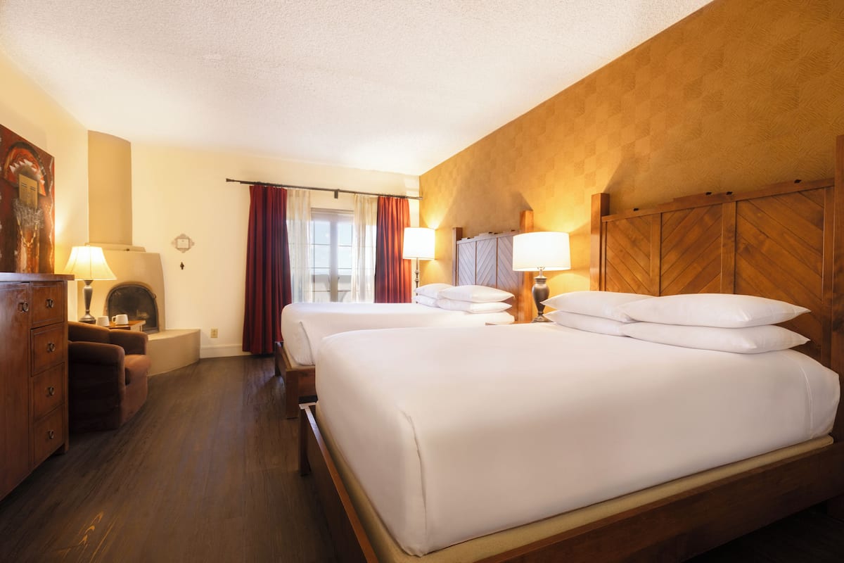 Habitación de hotel con dos camas, cabecera de madera, cómoda, lámpara y un cuadro en la pared.