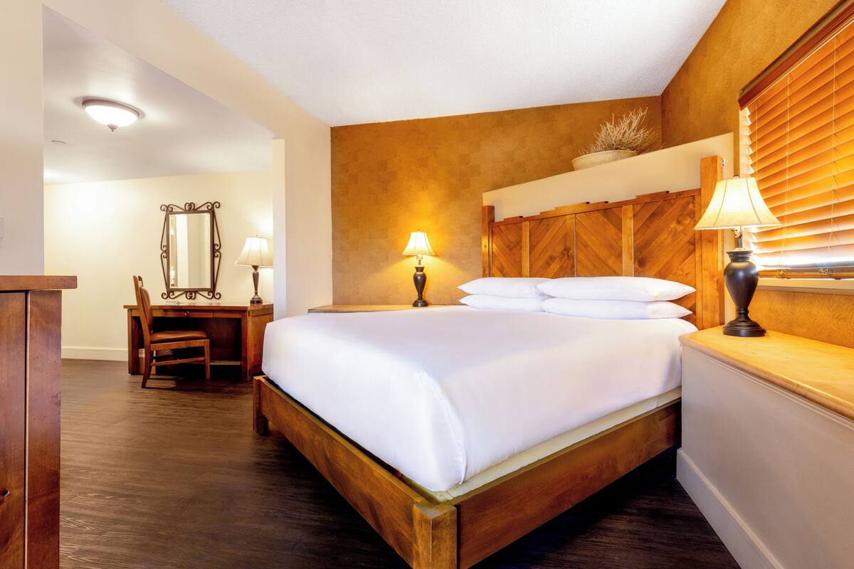 Habitación de hotel con una cama de madera, un escritorio con una silla, un espejo y dos lámparas de noche.