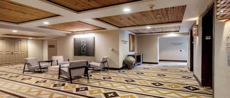 A hotel lobby with a patterned carpet, wooden ceiling, seating area, and directional signs.