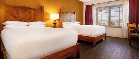 A hotel room with two wooden beds, a nightstand with a lamp, a window with curtains, and a wooden chair.