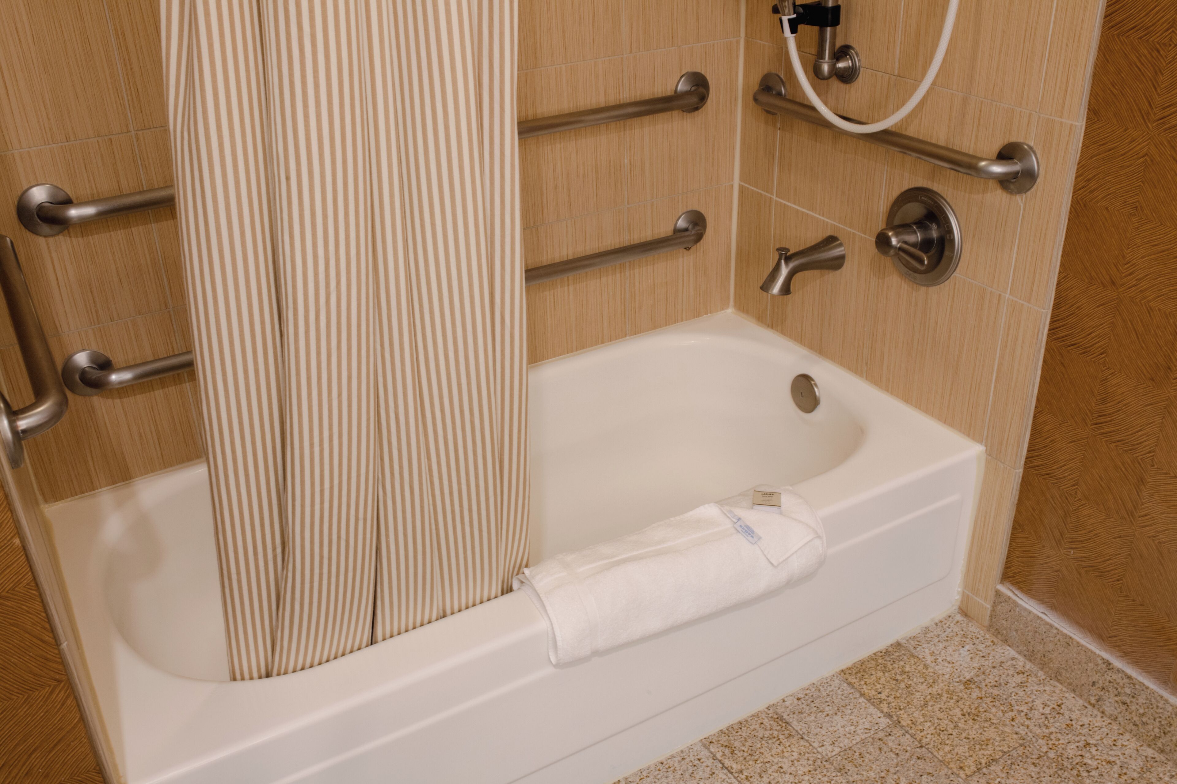 A bathroom with a bathtub, grab bars, a shower curtain, and a towel.