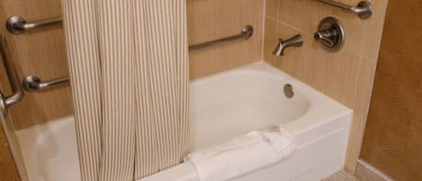 A bathroom with a bathtub, grab bars, a shower curtain, and a towel.
