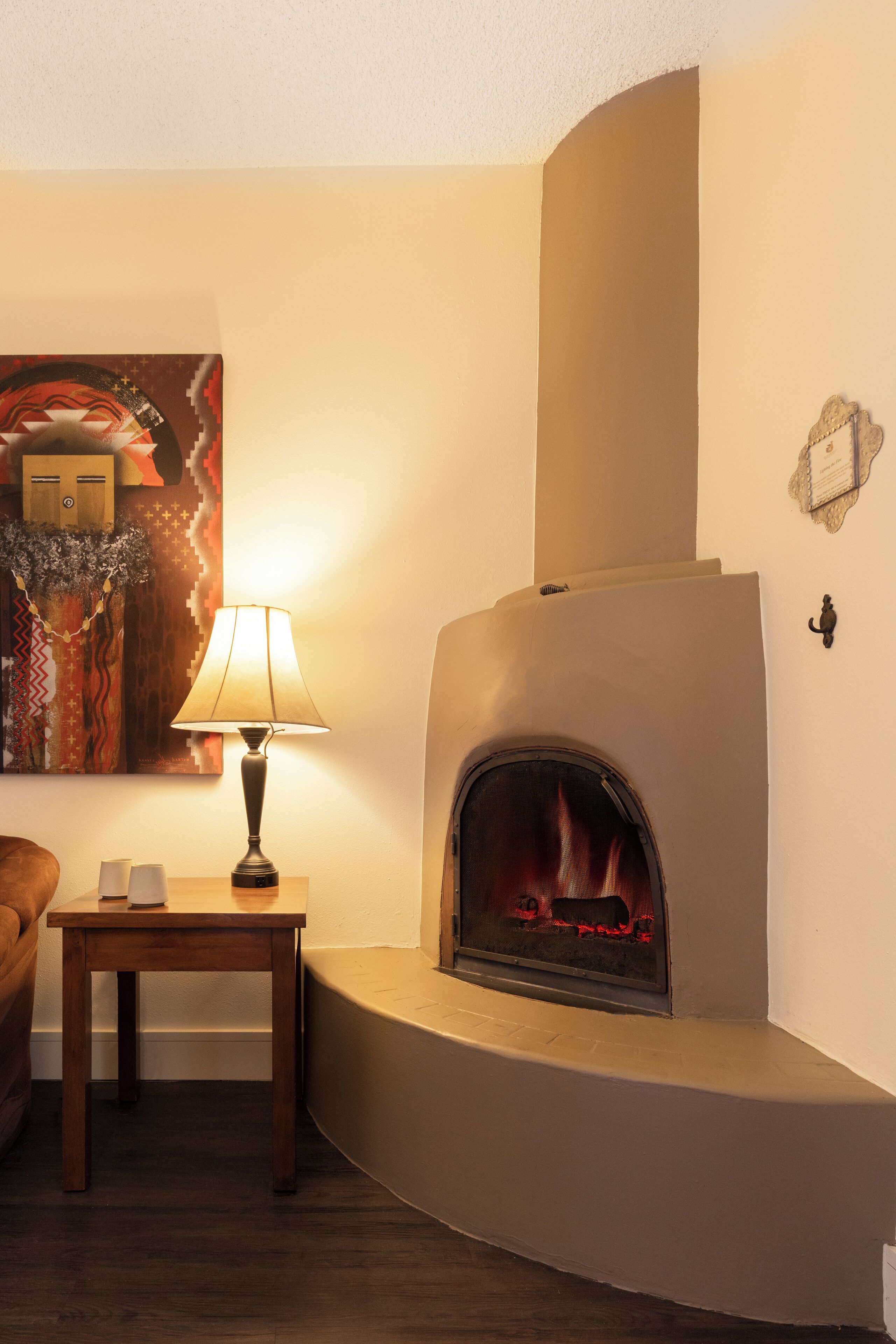 A cozy living room with a fireplace, a wooden table, and a lamp.