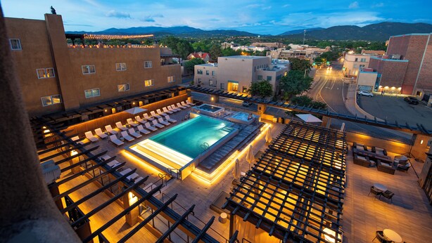 A rooftop pool area with lounge chairs and a hot tub, surrounded by buildings and a view of the mountains. - Eldorado Hotel & Spa (Santa Fe)