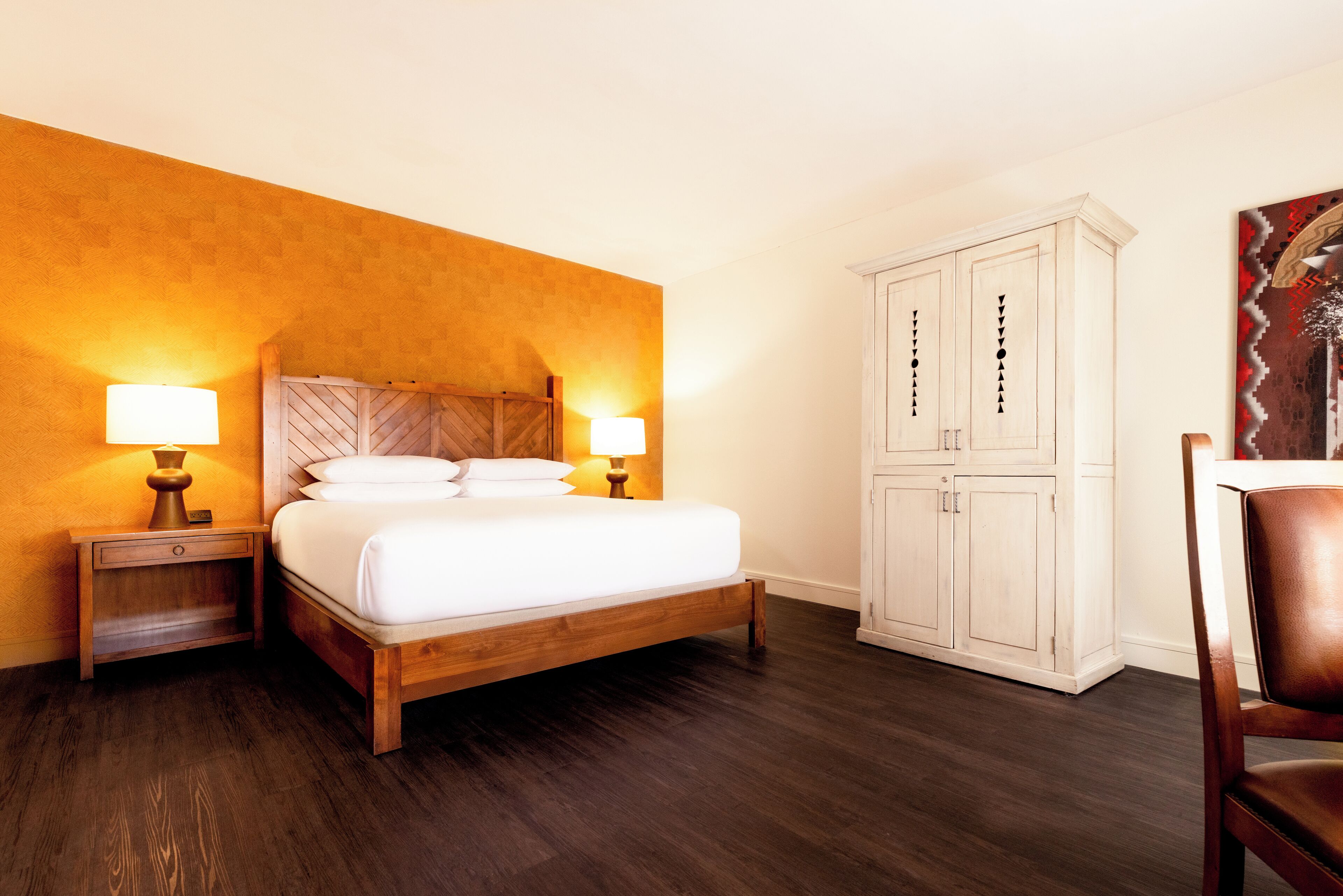 A hotel room with a wooden bed, two bedside lamps, a wardrobe, and a chair.