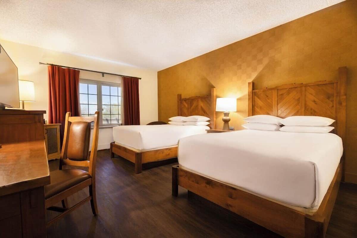 Habitación de hotel con dos camas, un escritorio, una silla y una ventana con cortinas.