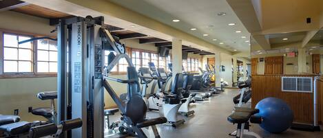 A gym with various exercise machines, a large exercise ball, and a mirrored wall.
