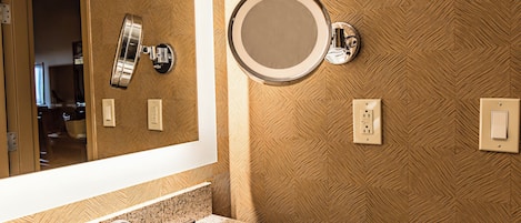 A bathroom with a granite countertop sink, a mirror, a wall-mounted light, and a power outlet.