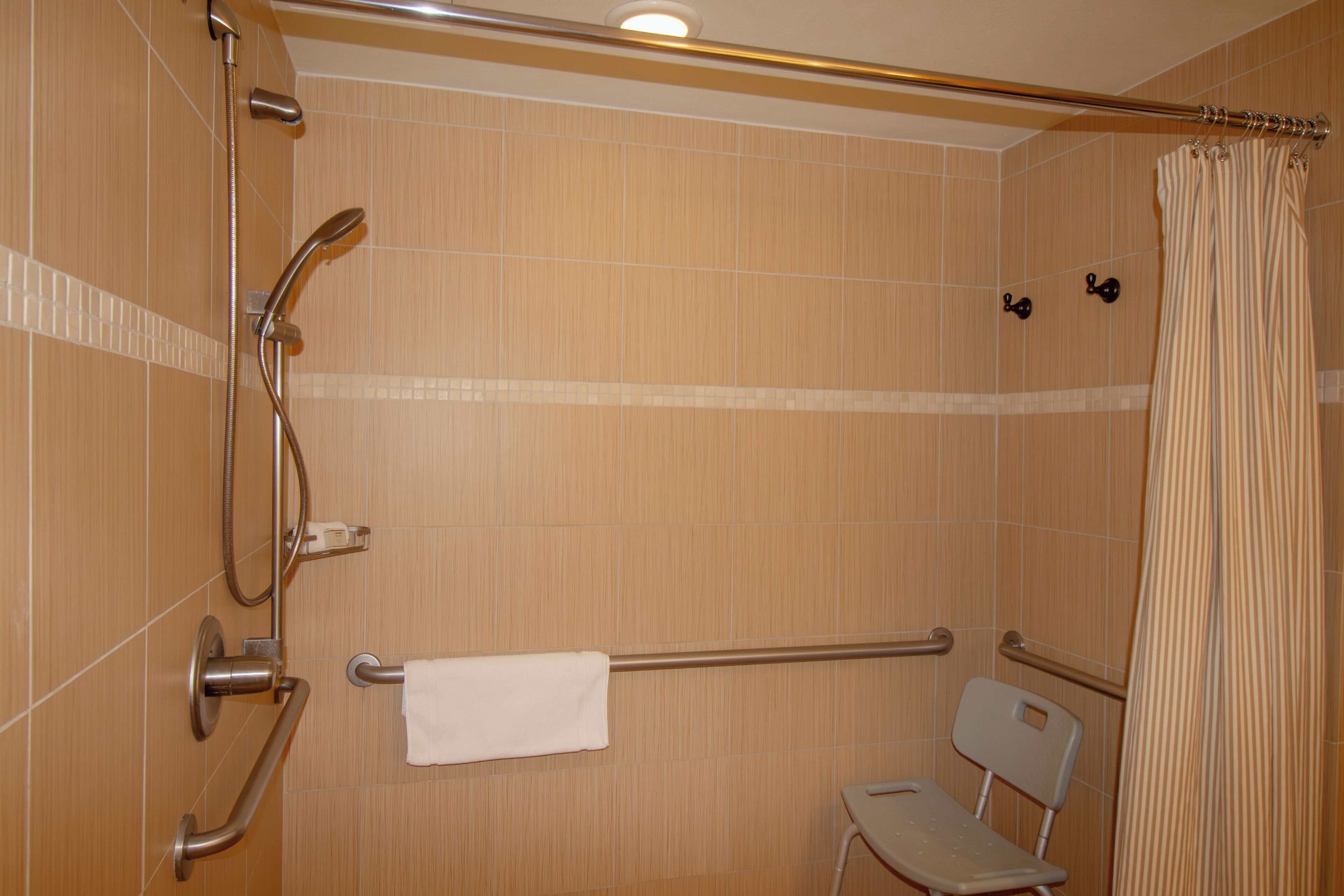 A bathroom with a shower, grab bars, a towel rack, and a wheelchair-accessible chair.