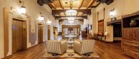 A spacious hotel lobby with wooden floors, a central seating area, and a high ceiling with exposed beams.