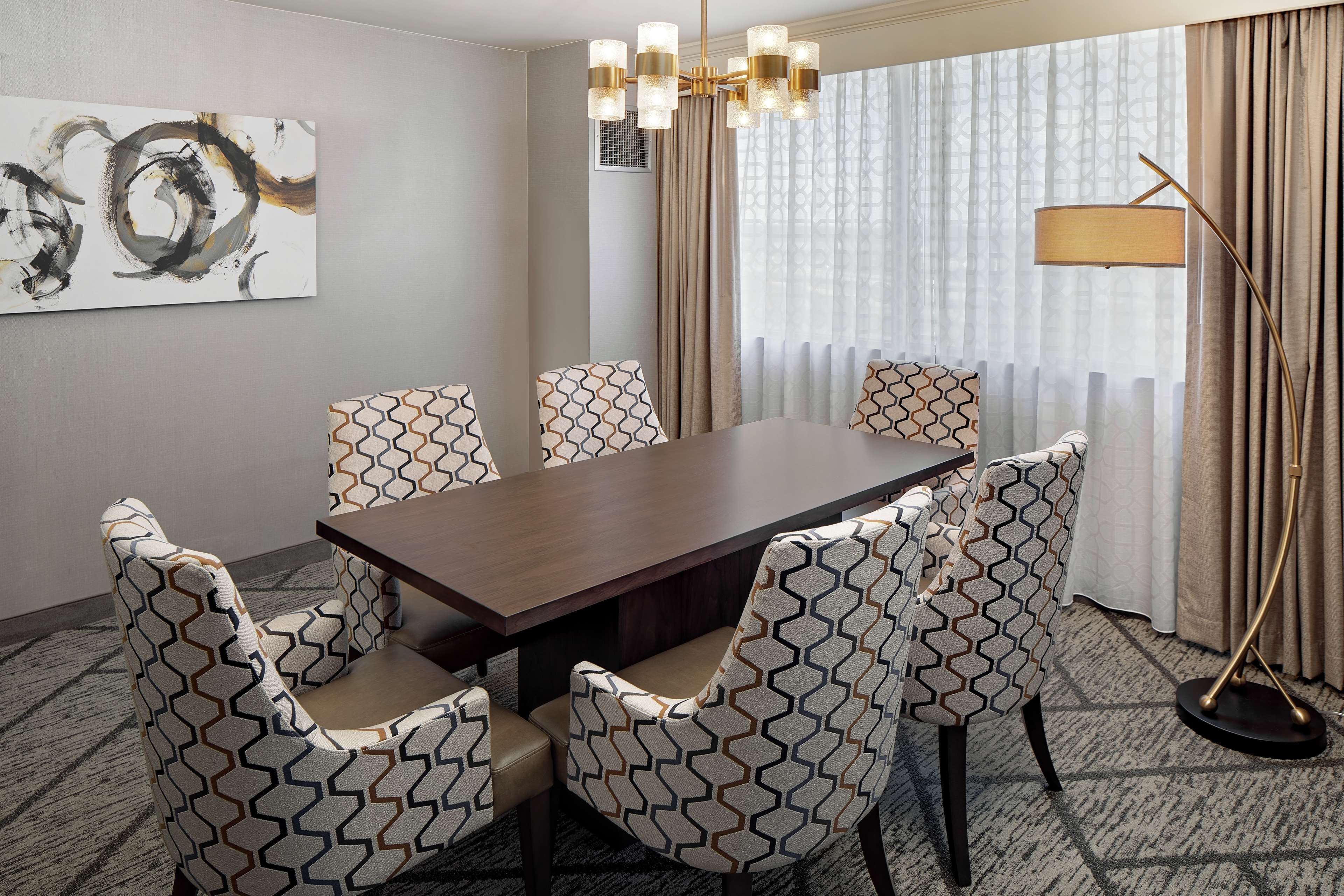 A conference room with a rectangular table, six patterned chairs, a modern chandelier, and a large abstract painting on the wall.