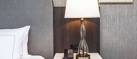Une chambre d’hôtel avec un lit, une table de chevet avec une lampe, une télécommande et un petit appareil électronique.