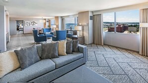 Habitación de hotel con un sofá gris, sillones azules y un ventanal con vistas a la ciudad.