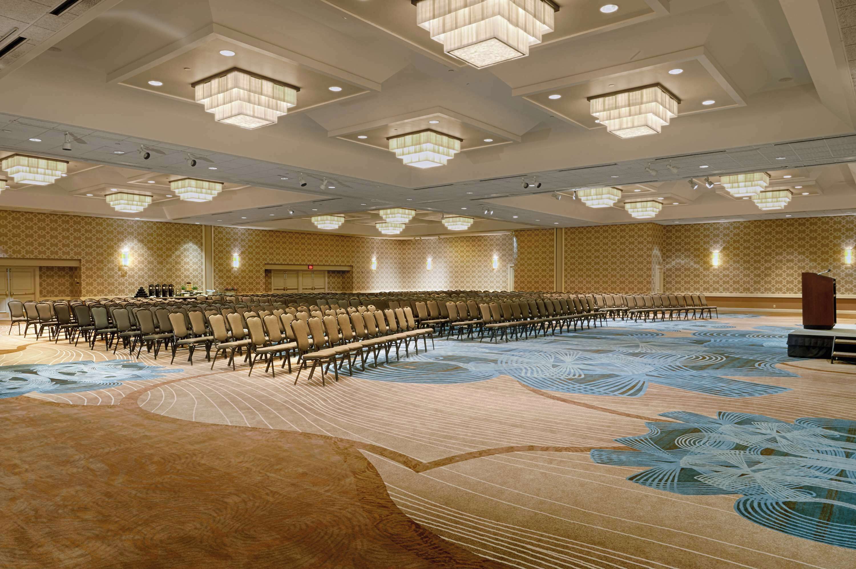 A large conference room with rows of chairs, a stage, and a patterned carpet.