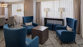 Een moderne hotelkamer met blauwe fauteuils, een donkerhouten salontafel en een kamerbreed tapijt met dessin.