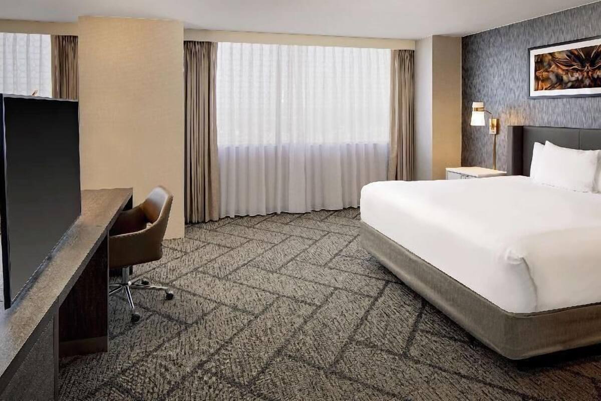 Ett hotellrum med en säng, ett skrivbord, en stol, en tv och ett fönster med gardiner.