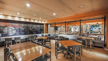 A restaurant with wooden tables and chairs, a large mural on the wall, and a view of the kitchen through the windows.