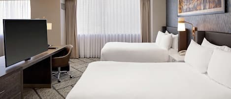 A hotel room with two beds, a desk, a TV, and a painting on the wall.